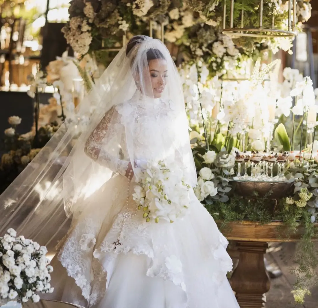 Noiva com vestido de renda e véu em jardim iluminado
