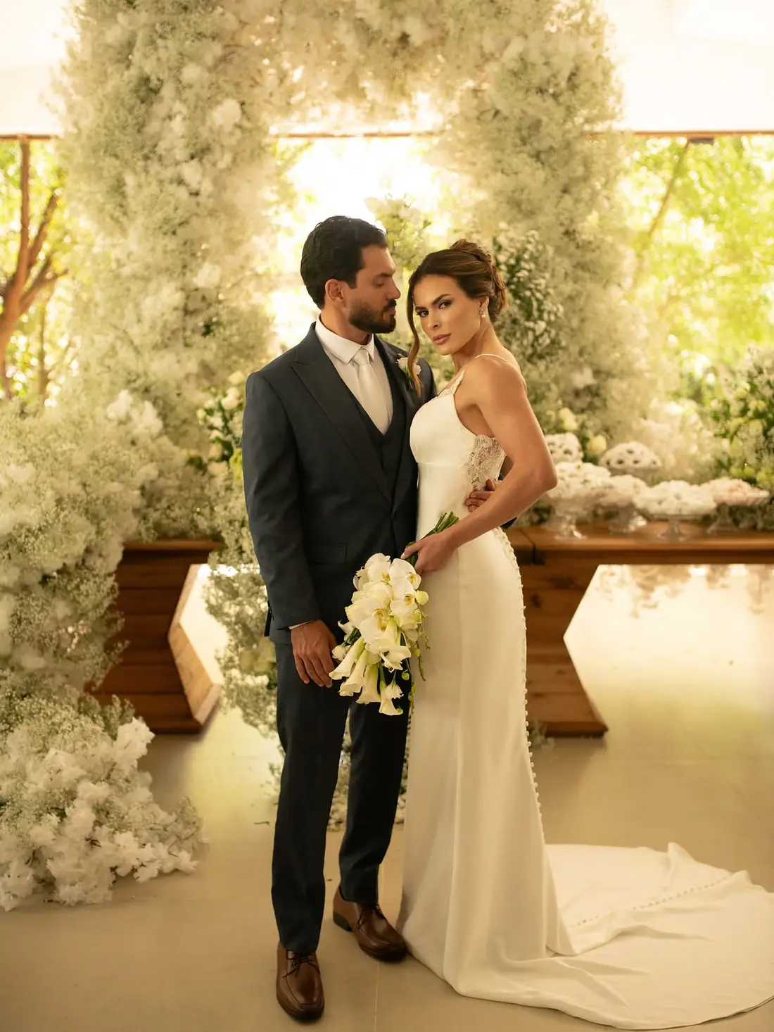 Noivos sob arco floral branco no dia do casamento